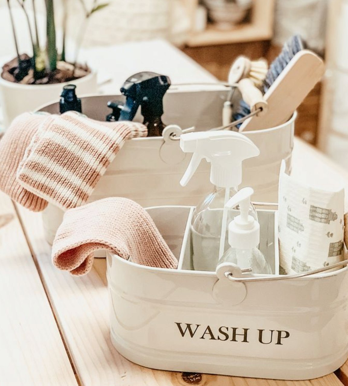 A cream cleaning caddy with sprays, brushes and soft pink cloths, ready for a White as Snow home clean